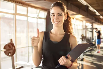 Foto op Canvas Personal trainer or fitness instructor holding a clipboard and showing thumbs up in gym. © Bojan