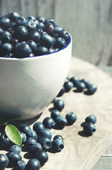 Juicy berries of bilberry in a cup on a wooden surface, close up