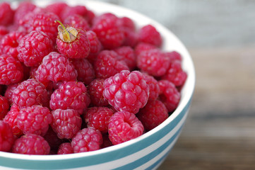 Juicy berries of raspberry in a bowl on a wooden surface, close up