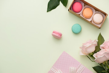 French macaroons. Many variegated sweet macarons in box with bouquet of pink roses on the table