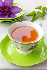 Tea in a cup of green and a bud of clematis colors in a rural style on a light background with a copy space