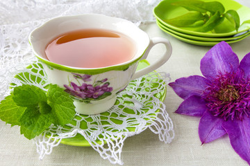 Obraz na płótnie Canvas Tea in a cup of green and a bud of clematis colors in a rural style on a light background with a copy space