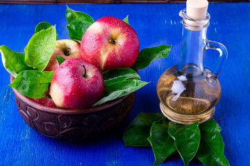 Apple cider vinegar in glass bottle on blue background. Red apples in brown bowl.