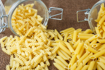 Italian pasta - penne and fusilli in glass jar on brown background