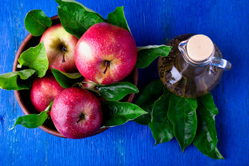 Apple cider vinegar in glass bottle on blue background. Red apples in brown bowl. Top view.