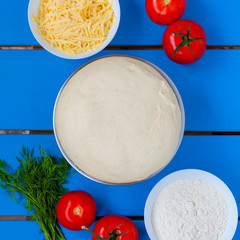 Pizza dough with ingredients on blue wooden table.