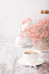 White cup of coffee with pink flowers on old white wooden background with copy space.