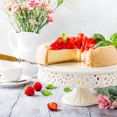 Piece of delicious homemade strawberry cheesecake and flowers on gray stone background. Selective focus.