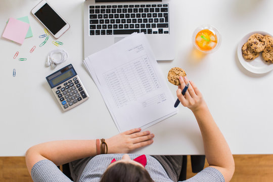 Woman With Tax Report Eating Cookie At Office