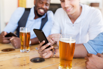 male friends with smartphone drinking beer at bar