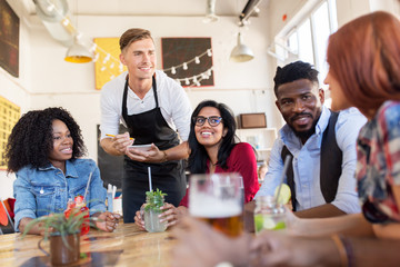 waiter and friends with menu and drinks at bar
