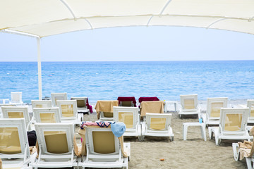 White plastic sunbeds in sandy beach under big parasol