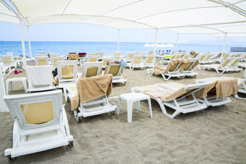 White plastic sunbeds in sandy beach under big parasol