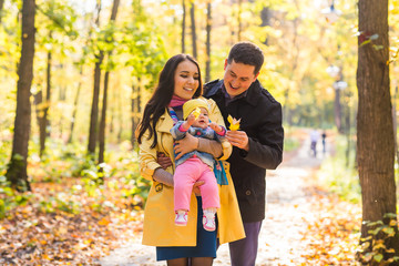 Naklejka premium Happy young family in the autumn park outdoors on a sunny day. Mother, father and their little baby girl are walking in the park. Love and family concept.