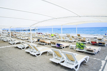 White plastic sunbeds in sandy beach under big parasol