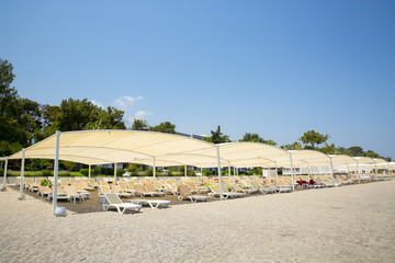 White plastic sunbeds in sandy beach under big parasol