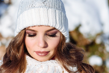 close up Winter portrait of a Happy candid beautiful young lady in a white knitted beanie hat and gloves