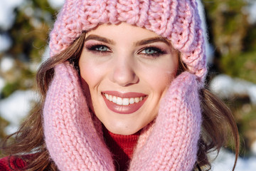 close up Winter portrait of a Happy candid beautiful young lady in a pink knitted beanie hat and gloves