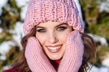 close up Winter portrait of a Happy candid beautiful young lady in a pink knitted beanie hat and gloves