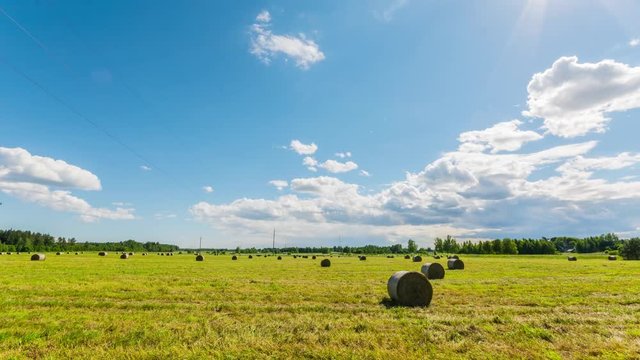 Timelapse of summer meadow with hay bales under blue sky with clouds. Timelaspe footage.