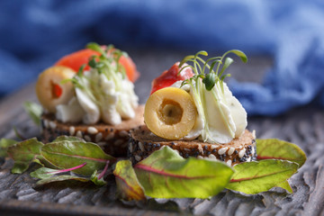 Delicious canape with salmon, cottage cheese, olive with micro greens on a dark background. Cold appetizer.