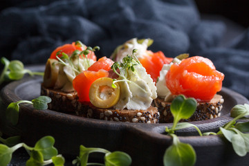 Delicious canape with salmon, cottage cheese, olive with micro greens on a dark background. Cold appetizer.