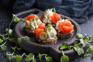 Delicious canape with salmon, cottage cheese, olive with micro greens on a dark background. Cold appetizer.