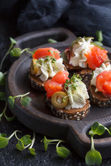 Delicious canape with salmon, cottage cheese, olive with micro greens on a dark background. Cold appetizer.
