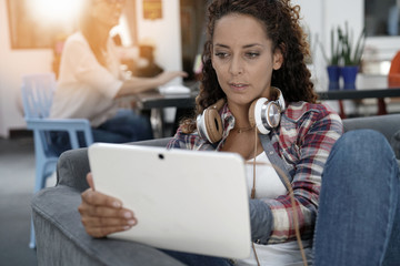 Trendy girl sitting in sofa with tablet and headphones