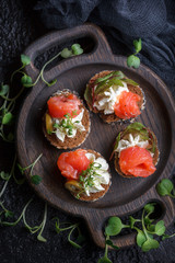 Delicious canape with salmon, cottage cheese, olive with micro greens on a dark background. Cold appetizer.