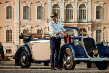 Confident wealthy young man with briefcase near classic convertible
