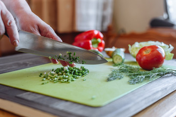 Cut green onion with a kitchen knife on a wooden cutting board. Fresh green onions on a cutting board. Cutted Green Onions On Wooden Cutting Board