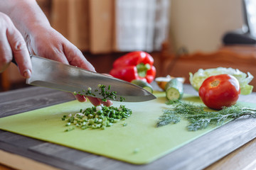 Cut green onion with a kitchen knife on a wooden cutting board. Fresh green onions on a cutting board. Cutted Green Onions On Wooden Cutting Board