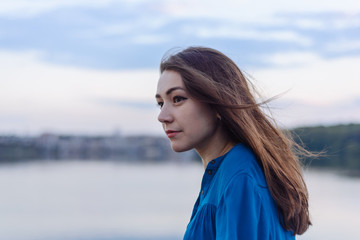 Summer happy portrait beautiful woman girl caucasian asian blended in blue shirt posing on background sky lake water sunset long hair brunette outdoors
