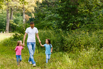 Naklejka na ściany i meble Father and two little daughters are walking in the park
