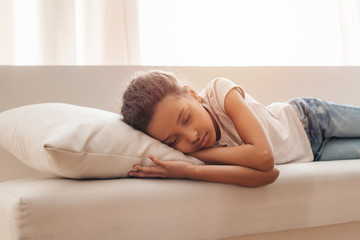 Adorable little african american girl sleeping on sofa at home