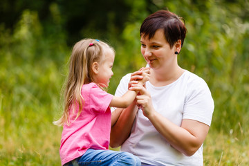 Fototapeta premium Daughter mother paints her lips lipstick. Family walk in a park.