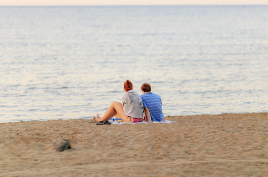 A girl and a young man sit on the beach in the evening on the sand