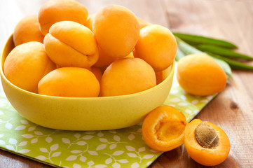 Tasty apricot with leaves lie on a wooden board. Heap of apricots in wooden bowl on table