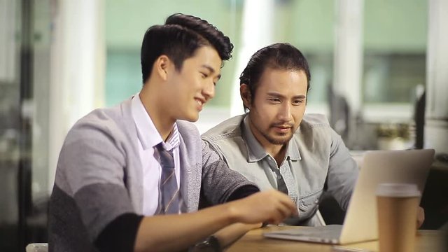 two asian businessmen working together in office using laptop computer