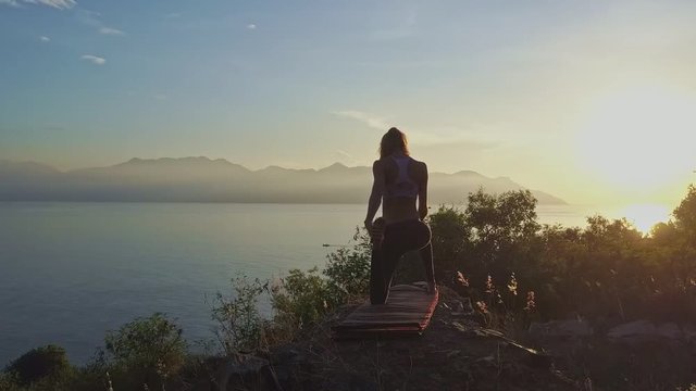 Motion around Slim Girl Doing Yoga Asanas on Steep Cliff at Dawn