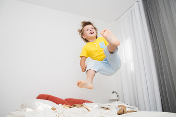 Cheerful little boy  jumping on bed at home
