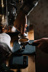 The process of making coffee step by step. Man tamping freshly ground coffee beans in a portafilter on a working wooden table