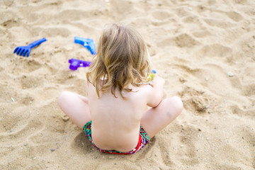 Kind mit blondem Haar spielt am Strand im Sand
