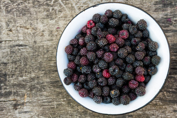 Ripe blackberries in rustic bowl on old wooden background. Top view