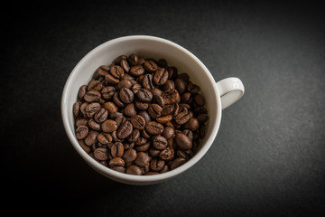 Roasted coffee beans in white cup on dark background. Selective focus.