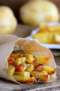 Crispy fried potatoes with spices. Delicious fried potatoes in paper and on a wooden table. Simple potato recipe. Vertical photo
