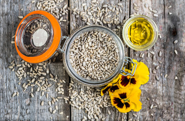 Glass of oil from sunflower seeds in rustic jar on wooden table, flat lay from above
