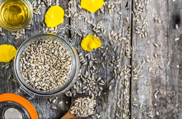 Glass of oil from sunflower seeds in rustic jar on wooden table, flat lay from above