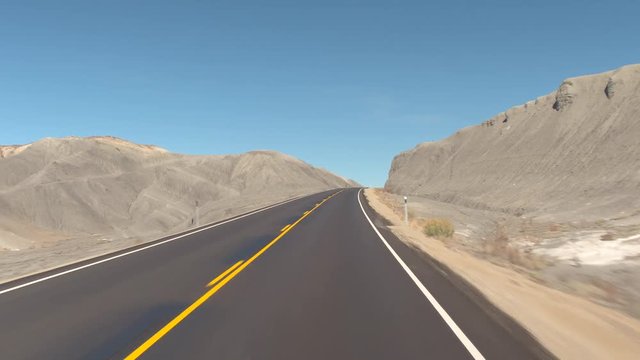 FIRST PERSON VIEW: Driving along an empty road past a grey sandstone mountains in Utah canyon, USA. Traveling on road trough rocky desert, exploring nature on sunny day. Road trip across United States